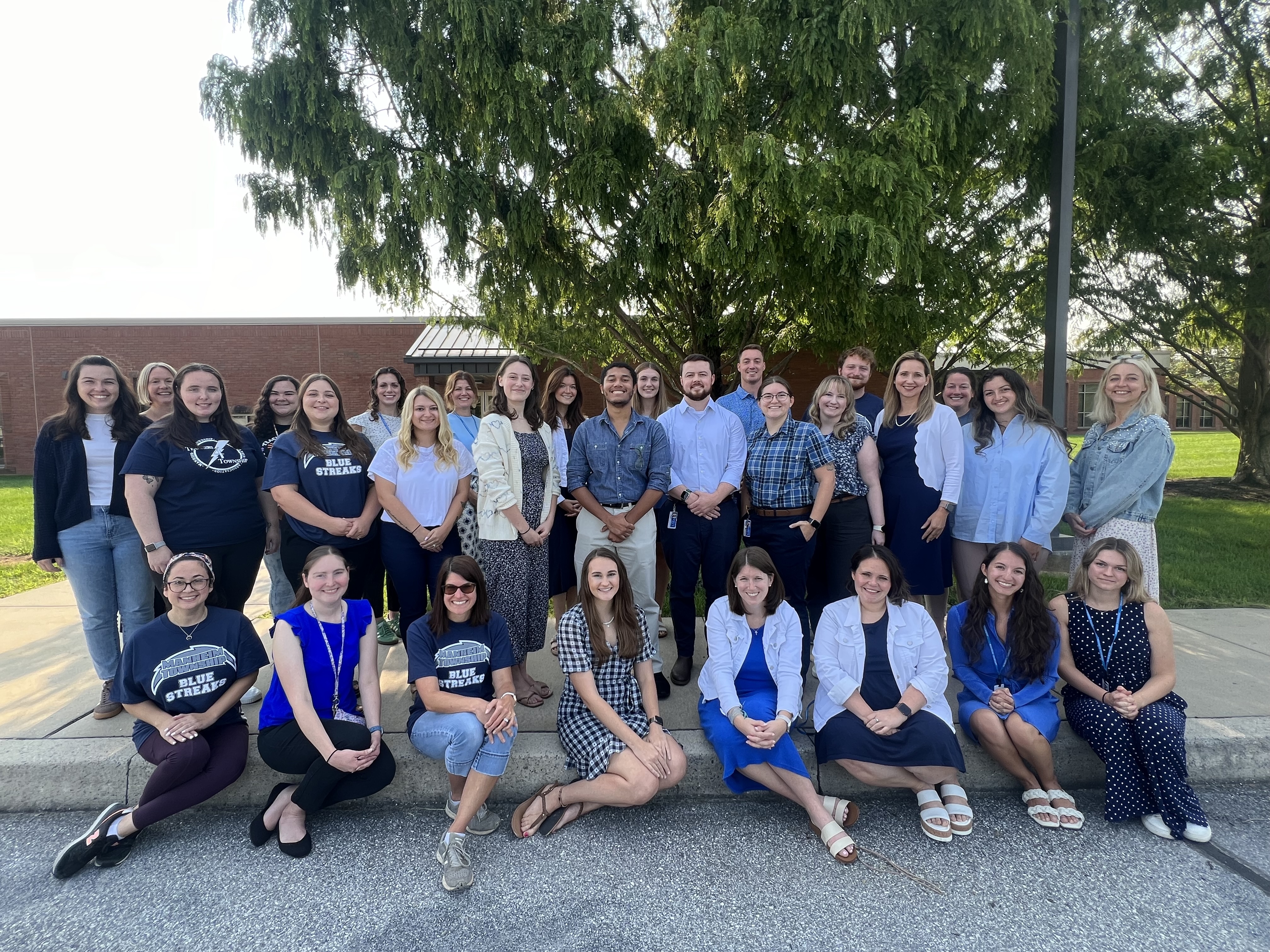 New teachers and staff standing under a tree outside of the District Office 